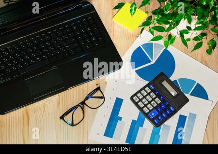 workstation da ufficio con computer portatile, calcolatrice e grafici su un ripiano in legno Foto Stock