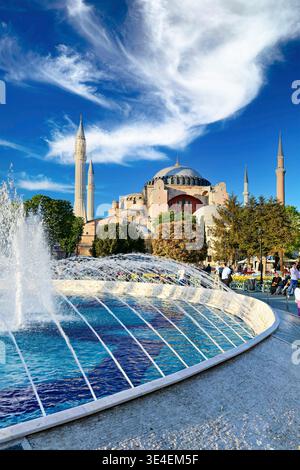 I visitatori esplorano la grande Moschea di Hagia Sophia a Istanbul. L'acqua spruzza da una fontana mentre il sole splende in questo sito storico. Foto Stock