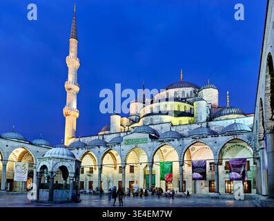 La gente cammina attraverso il cortile della Moschea Blu di Istanbul. La moschea si erge alta con le sue cupole e minareti al calare della notte. Foto Stock