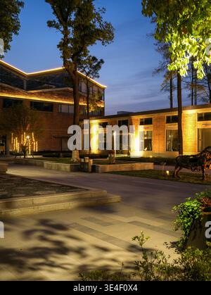 Wuhan, Cina - 5 aprile 2025: Passaggio pubblico pavimentato circondato da giardini e storici edifici in mattoni rossi illuminati di notte. L'immagine mostra a. Foto Stock