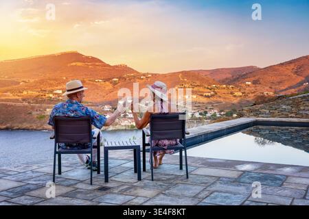 Una coppia di anziani si siede insieme vicino alla piscina e si gode il tramonto estivo con un bicchiere di vino Foto Stock
