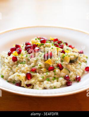 Risotto cremoso con semi di melograno ed erbe fresche servito in una ciotola bianca Foto Stock
