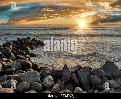 Spettacolare tramonto sull'oceano visto da una scogliera rocciosa, con raggi di sole che penetrano attraverso le nuvole e si riflettono sulle onde della costa namibiana Foto Stock