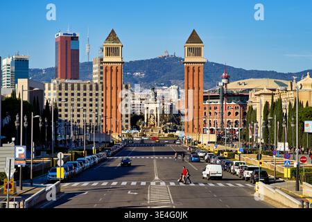 Le persone camminano e le auto guidano sulla strada in Plaza de Espana. Le torri si ergono alte con un cielo blu chiaro sullo sfondo. Foto Stock
