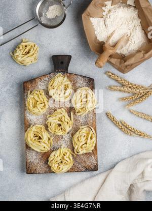 Cibo, tagliatelle. Pasta cruda cruda italiana tradizionale fatta in casa su una tavola di legno su sfondo grigio di cemento. Messa a fuoco selettiva Foto Stock