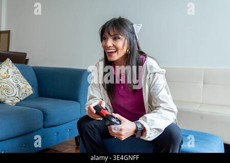 Donna che gioca a un videogame, ridendo e si sente eccitata in salotto Foto Stock