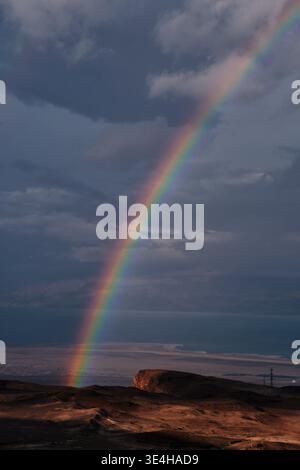 Un luminoso arcobaleno sul suggestivo paesaggio desertico con nuvole di tempesta e mare calmo sullo sfondo. Suggestivo scenario naturale con luci colorate Foto Stock