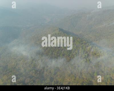 Vista aerea devastante che cattura il fumo intenso dagli incendi estivi che si diffondono attraverso la lussureggiante foresta verde e il paesaggio montano di mai Thailand causando un Foto Stock