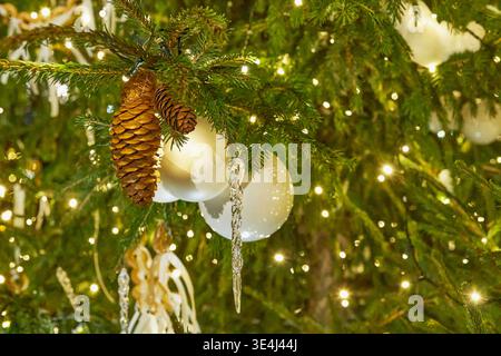 Primo piano di alberi di Natale decorati con coni di pino, ornamenti bianchi e calde luci festive Foto Stock