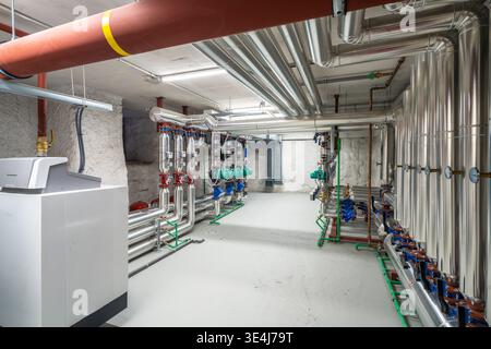 Interno luminoso e moderno della sala caldaie con tubazioni metalliche isolate, valvole, pompe e condotti di ventilazione in un seminterrato dell'edificio, che mostra l'HVA industriale Foto Stock