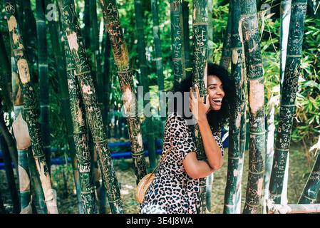 Allegra giovane donna sorridente tra gli alti bambù in un bellissimo giardino marocchino, godendosi un momento di calma all'aperto con vegetazione naturale, atmosfera di viaggio, e. Foto Stock