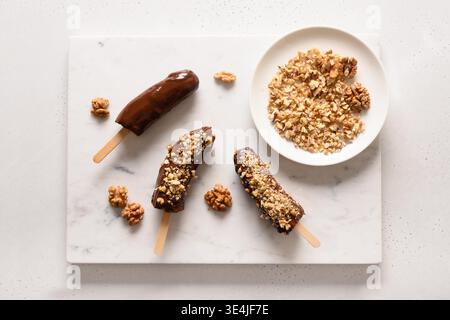 Lecca di banana surgelata o lecci con noci spruzzare per i bambini su bianco. Dolci vegani facili. Vista dall'alto. Foto Stock