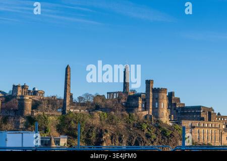 Vista panoramica di Calton Hill a Edimburgo, con monumenti storici in pietra, un obelisco, un'alta torre e rovine classiche immerse nel caldo tardo pomeriggio Foto Stock