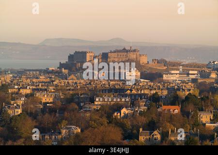 Il castello di Edimburgo domina lo skyline mentre la calda luce dell'ora d'oro inonda gli edifici storici in pietra e i tetti residenziali, fotografati da Blackford Foto Stock