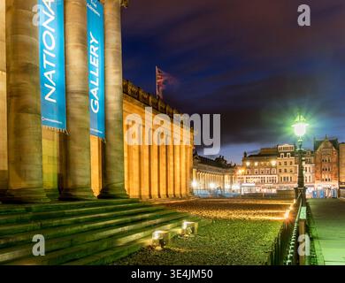 La National Gallery of Scotland di Edimburgo è immersa nella calda luce della sera, con colonne classiche, gradini in pietra e un'illuminante lampada da strada Foto Stock