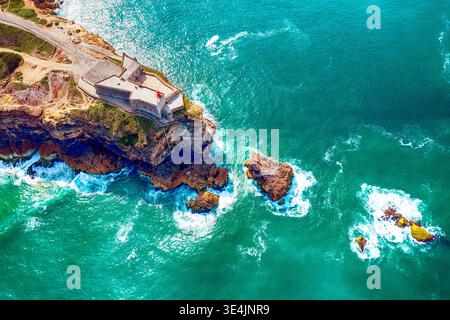 Rocky Cape con un faro nella città di Nazare in Portogallo sulle rive dell'Oceano Atlantico Foto Stock
