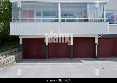 Casa moderna con balcone in vetro e porte rosse del garage. La ringhiera in metallo bianco contrasta con le porte rosse profonde. Foto Stock