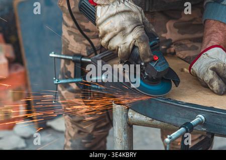 Primo piano di un lavoratore esperto che utilizza una smerigliatrice angolare per lavorare metallo con scintille brillanti che volano. Concentrati sulle mani, sulla precisione e sulla cura artigianale. Concetto di ma Foto Stock