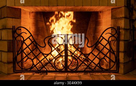 fiamme in un camino di casa in mattoni con una griglia forgiata in metallo, con illuminazione soffusa Foto Stock