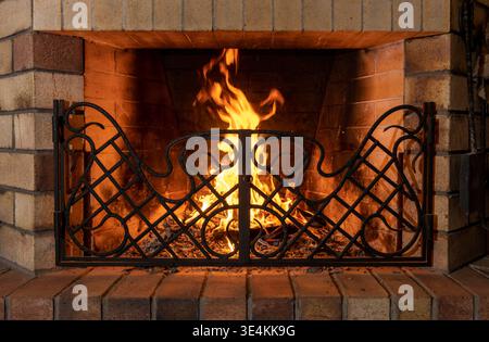 fiamme in un camino di casa in mattoni con una griglia forgiata in metallo, con illuminazione soffusa Foto Stock