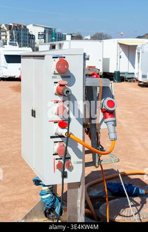 Montante portatile per utenze con prese di alimentazione industriali accanto ai punti di accesso aperti per la manutenzione in un'area temporanea di caravan e supporto del rimorchio su un terreno polveroso Foto Stock