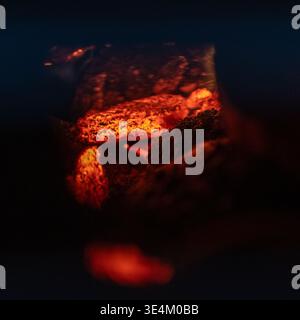 Carboni ardenti e brace incandescente bruciano con un profondo bagliore arancione su uno sfondo scuro e suggestivo all'interno di un barbecue o di un camino. Foto Stock