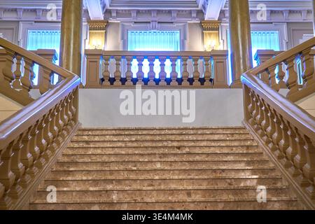 Una grande scalinata in marmo biforcato con ringhiere in legno ornate e balaustre all'interno di un edificio storico. La scala simmetrica presenta Foto Stock