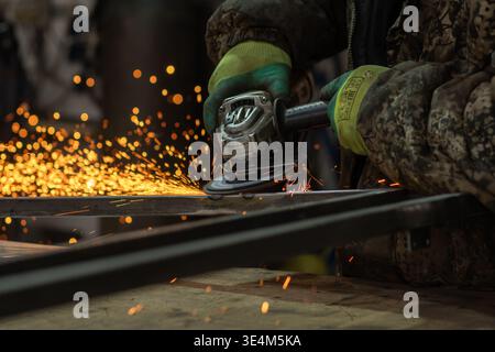 Un abile artigiano maschio che rettifica con precisione il metallo e crea scintille in un ambiente di officina Foto Stock