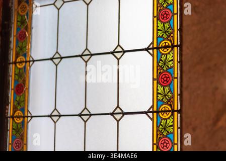 Primo piano di vetrate colorate vintage con pannelli geometrici in piombo e bordo floreale colorato, delicatamente illuminato con profondità di campo bassa. Foto Stock