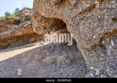 Vista ravvicinata di una formazione rocciosa sedimentaria caratterizzata da una piccola cavità simile a una grotta o cavità. La superficie rocciosa del conglomerato presenta un aspetto ruvido Foto Stock