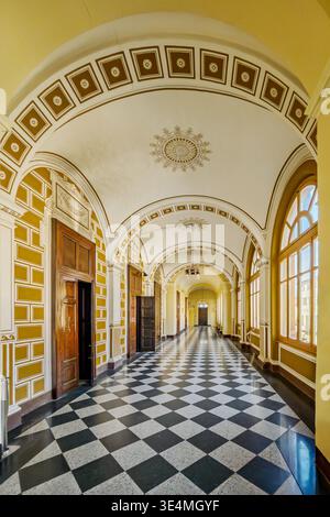 Elegante corridoio con volta a botte decorata, pavimento a scacchi bianco e nero e finestre ad arco, situato in un edificio con eclettici archi italiani Foto Stock