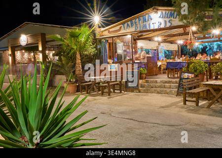 Ingresso alla Taverna Dimitris di notte ad Agia Galini, Creta. Intimo posto a sedere all'aperto con tavoli in legno, palme e calda illuminazione serale. Foto Stock