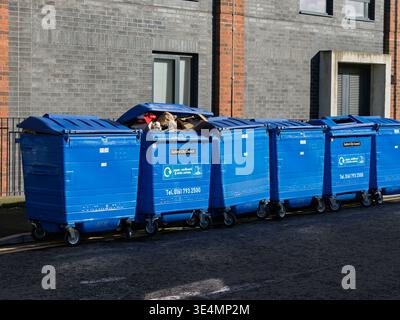 Salford, Manchester, Regno Unito, 28 marzo 2026: I cassonetti di cassonetti blu forniti dal consiglio di Salford formano un edificio in mattoni sotto un cielo limpido. Foto Stock