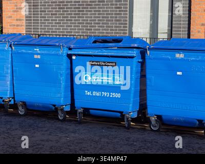 Salford, Manchester, Regno Unito, 28 marzo 2026: Contenitori di riciclaggio blu forniti dal consiglio di Salford allineati contro un edificio in mattoni. Foto Stock