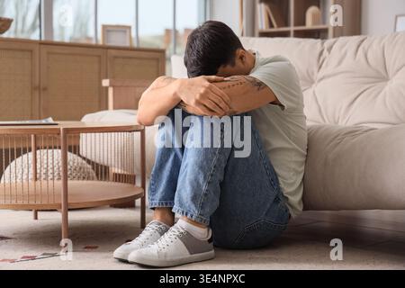 Giovane preoccupato seduto a terra a casa Foto Stock