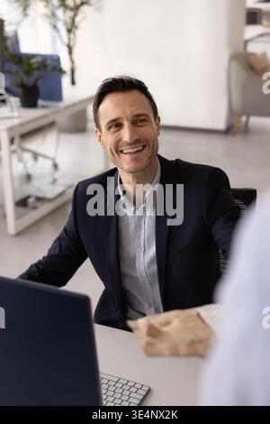 Un uomo d'affari sorridente seduto alla scrivania a prendere il pacco dalle mani della segretaria Foto Stock