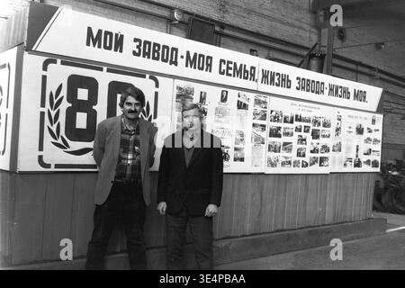Sloviansk, 1995 anni. Raccordi e impianti isolanti (AIZ). Due dipendenti maschi si trovano nell'area del comitato sindacale accanto a una grande bacheca aziendale con la scritta "My Plant - My Family". Lo stand visivo presenta fotografie d'archivio che celebrano l'ottantesimo anniversario dell'azienda. Questa suggestiva fotografia della metà degli anni novanta cattura splendidamente la forte identità industriale, l'orgoglio collettivo e il profondo rispetto per il patrimonio lavorativo, documentando la vibrante vita e la cultura della comunità pacifica del Donbas. Foto Stock