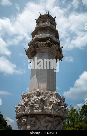L'antica colonna di pietra si erge su di un cielo blu brillante. Dettagli scolpiti adornano la base e la parte superiore a strati. Le nuvole si spostano delicatamente dietro la struttura. Sto Foto Stock