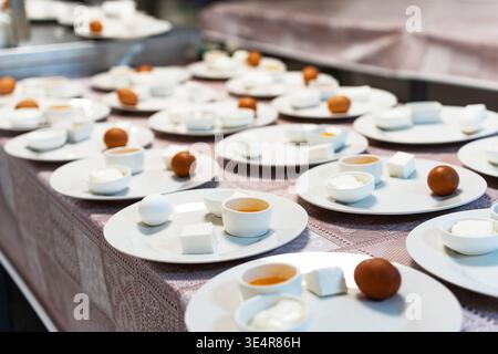 Un gran numero di piatti per la colazione per bambini a scuola o dipendenti di aziende. Su un piatto di uova, miele, formaggio e formaggio fresco Foto Stock