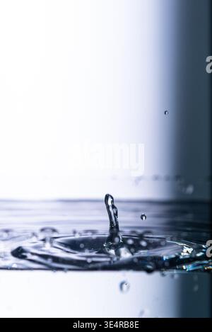 418.Una fotografia ad alta velocità di una goccia d'acqua che urta con la superficie dell'acqua, creando uno spruzzo simile a una colonna e spargendo increspature. L'immagine è Foto Stock