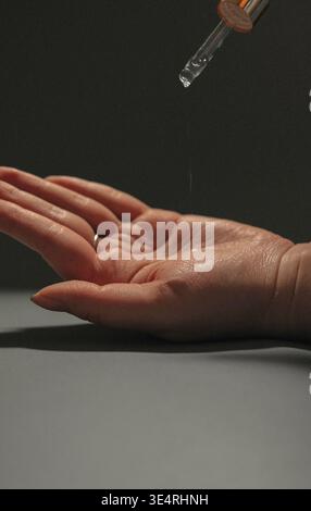 Primo piano della goccia di siero cosmetico che cade sulla mano dalla pipetta. Concetto di bellezza e cura della pelle. Foto Stock