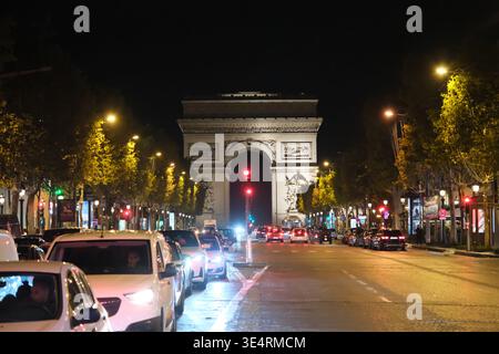 Parigi, Francia - 4 ottobre 2025: vista notturna dagli Champs-Élysées di Parigi, traffico stradale intenso e Arco di Trionfo illuminato in lontananza Foto Stock