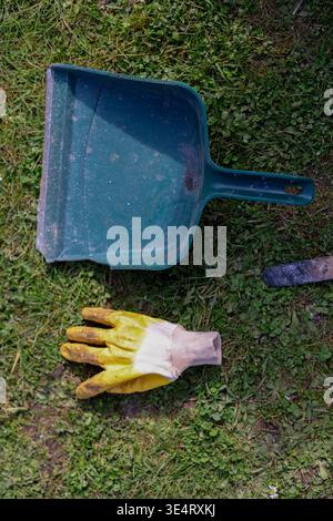 Utensili da giardino su erba con guanti e paletta, pulizia all'aperto e concetto di giardinaggio. Foto Stock
