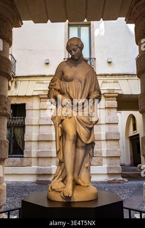 La scultura in marmo di una donna con un abbigliamento che scorre si erge graziosamente in un cortile, circondato da colonne di pietra e un edificio dai colori chiari a Verona Foto Stock