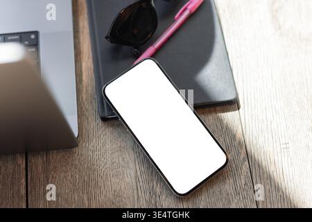 Mockup dello schermo del telefono sulla scrivania con il computer portatile. Accogliente ambiente da caffetteria, ideale per freelance, nomadi digitali o imprenditori online. Foto Stock