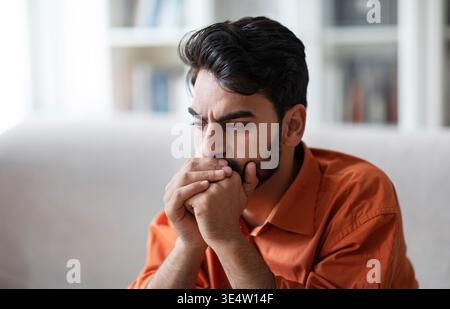 Primo piano di un triste uomo medio orientale seduto sul divano di casa Foto Stock