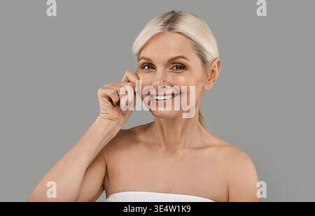 Concetto di rassodamento della pelle. Bella donna anziana che si tocca la faccia e sorride Foto Stock