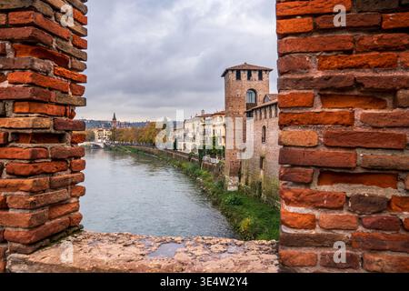 Vista suggestiva dell'Adige a Verona incorniciata dai mattoni rossi del Ponte Scaligero. L'immagine mostra le mura medievali di Castelvecchio Foto Stock