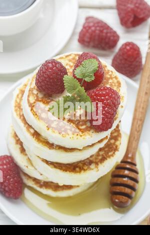 Cibo, pancake al formaggio fatti in casa con miele e lamponi freschi. Syrniki. Colazione tradizionale gustosa e salutare. Messa a fuoco selettiva Foto Stock