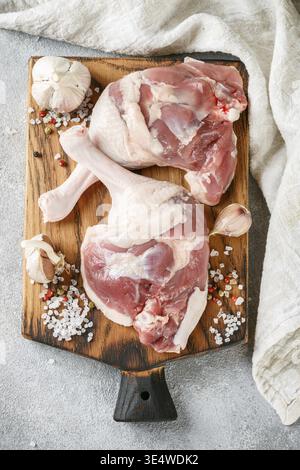 Cibo, carne di pollame cruda. Gambe d'anatra, aglio e spezie sale e pepe su un tagliere. Sfondo in cemento. Messa a fuoco selettiva e vista dall'alto Foto Stock